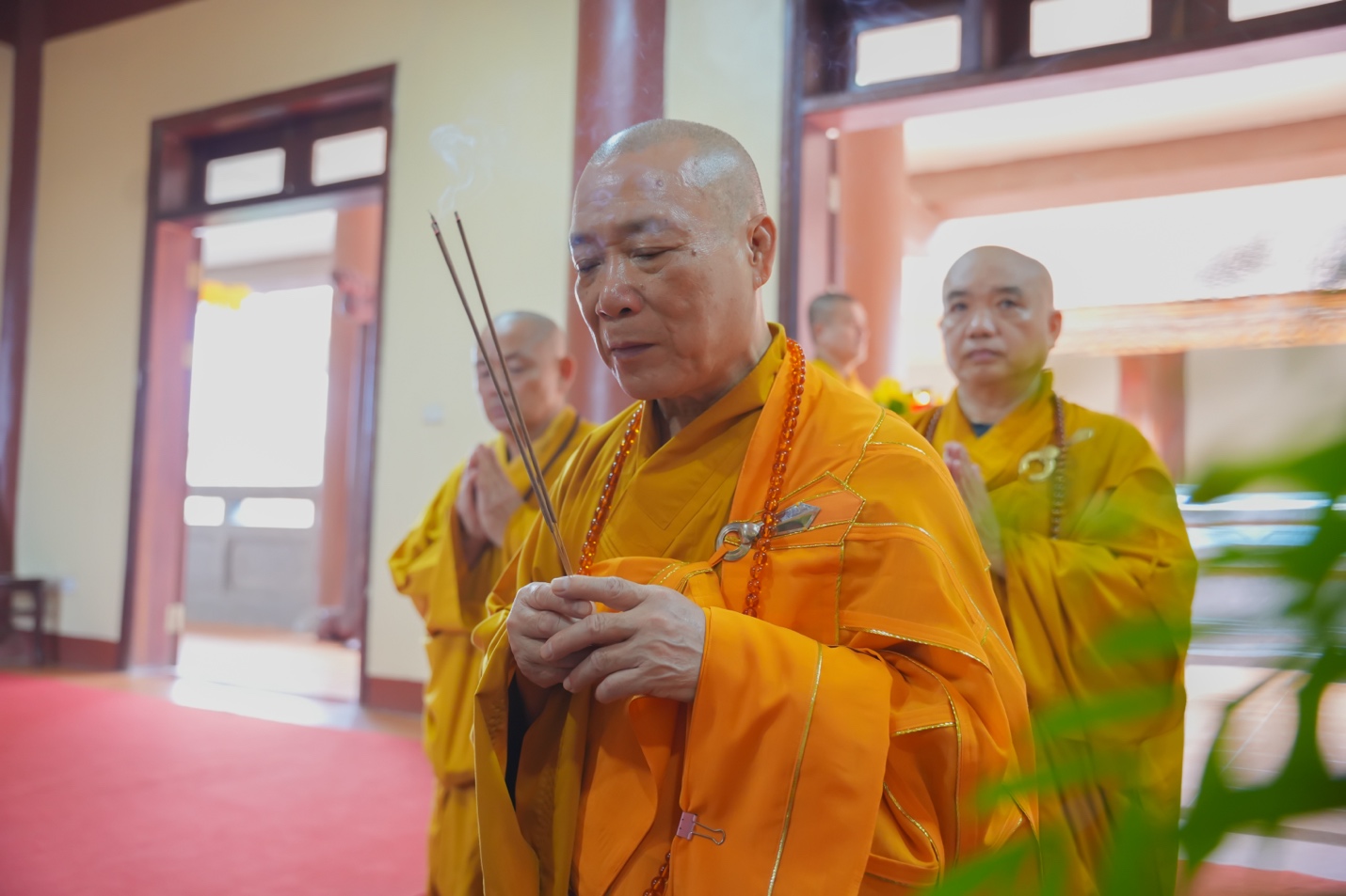 A group of men in orange robes holding incense sticks Description automatically generated