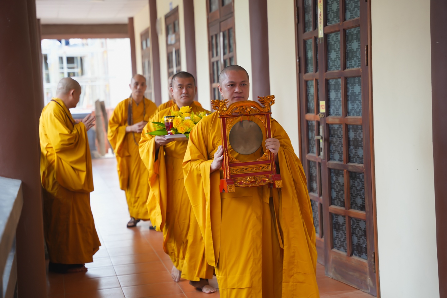 A group of people in yellow robes carrying a frame Description automatically generated