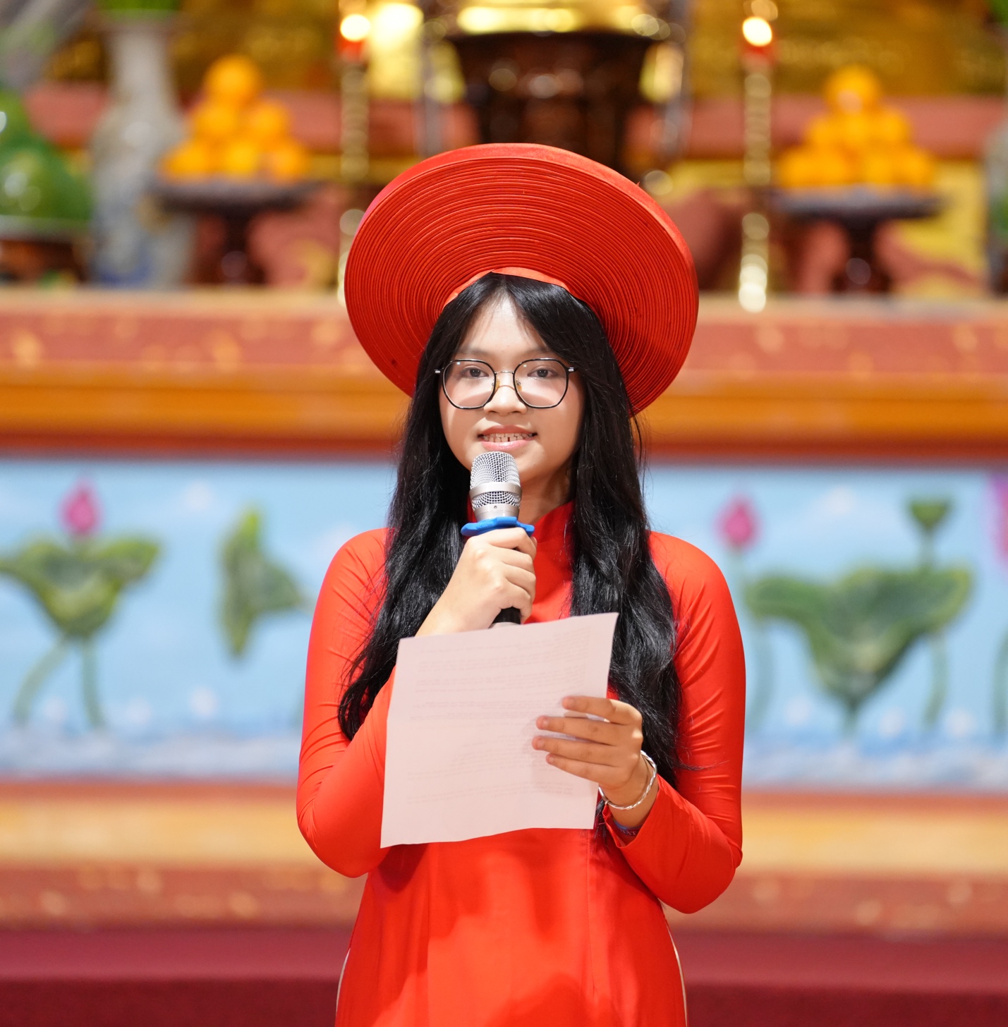 A person in a red dress holding a microphone and paper AI-generated content may be incorrect.