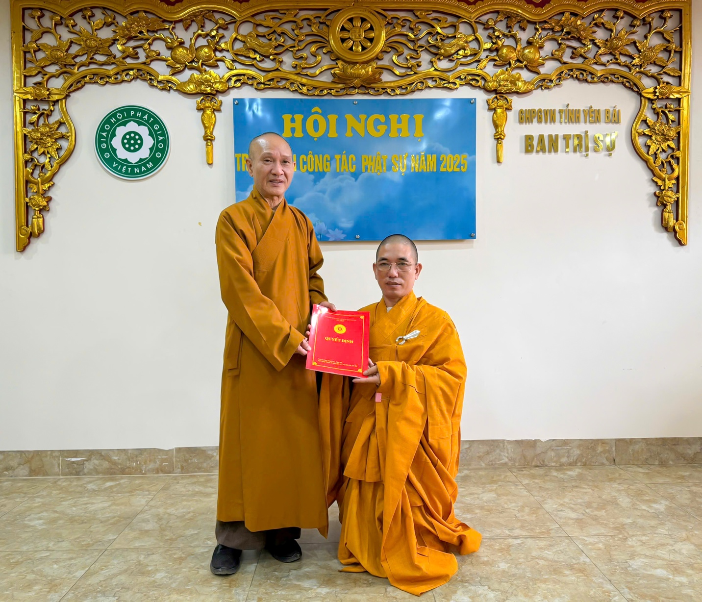 Two men in orange robes holding a red book AI-generated content may be incorrect.